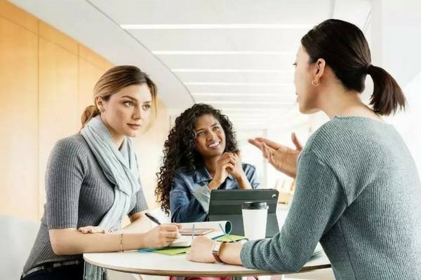 <p>3 women discussing around a table</p>